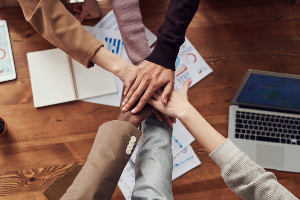 A group of people puts one arm in the center so that their hands are stacked over one another.